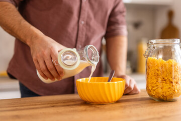 Man is preparing cereal for breakfast, pouring milk over a bowl of cereal in a cozy kitchen. everyday morning routine, evoking feelings of comfort, nourishment, and simplicity in the start of the day