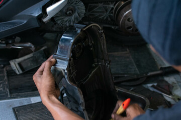 Close-up of a mechanic’s hands cleaning a scooter’s CVT housing using a special cleaning liquid during routine maintenance