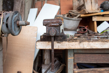 Old grinding machine mounted on a wooden workbench in an outdoor shed. Worn and rusted, it speaks of years of hands-on craftsmanship, sharpening tools and shaping materials.