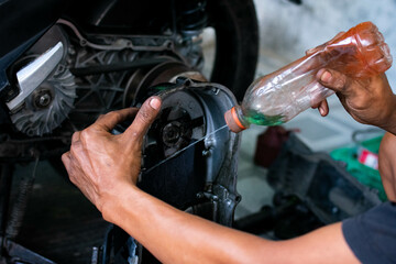 Close up of a mechanic’s hands cleaning a scooter’s CVT housing using a special cleaning liquid during routine maintenance