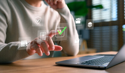 Man using laptop with virtual document management system and green check approval icon. Concept of paperless workflow, data validation, digital security, and business automation process.