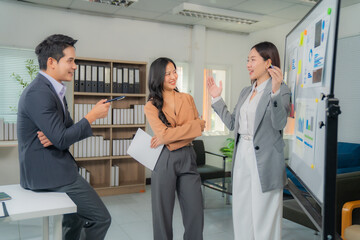 Three asian businesspeople are discussing strategy in the office during a meeting, using a...