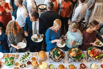 Diverse group at a buffet, enjoying food and conversation. People mingling, eating, and socializing at a lively gathering with a variety of dishes. People mingle at buffet and event.