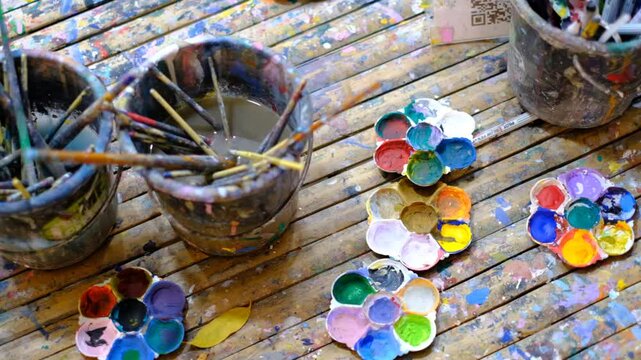 A table with paint brushes and paint pots. The paint pots are in different colors and sizes