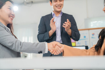 Two businesswomen shaking hands in a modern office, celebrating their successful deal as a...