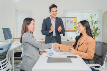 Two businesswomen shaking hands after closing a deal in the office while their manager applauding them, celebrating success and partnership