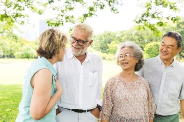 Naklejka premium Group of four seniors enjoying a sunny day in the park, smiling and chatting. Diverse elderly friends, outdoor gathering, happy and relaxed atmosphere. Group of elderly people friends in park.