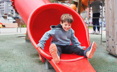 Happy boy sliding out of red playground tube outdoors