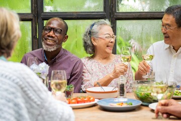 Group of diverse seniors enjoying a meal, laughing, and toasting with wine. Elderly friends, diverse gathering, joyful meal, and wine celebration. Diverse senior people drinking wine at lunch.
