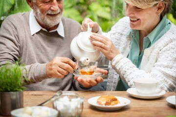 Retired couple enjoying tea. Senior man and woman sharing tea time. Happy elderly pair with tea, smiling and relaxed. Senior couple bonding over tea outdoors. Retired couple having tea.