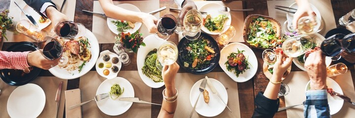 Top view of diverse hands toasting with wine over a table filled with food. Celebration, food, and wine create a festive atmosphere. Cheers and joy! Friends celebrating at a restaurant.