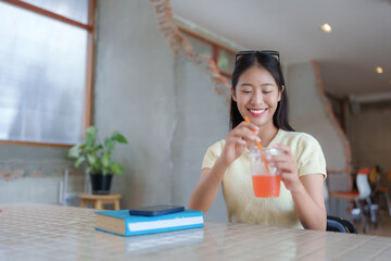 Young woman with glasses perched on her head smiles as she savors a refreshing drink at a cafe, her...