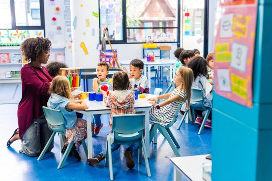 Diverse classroom with children and a teacher. Kids of various ethnicities learning together. Teacher guiding students in a colorful classroom setting. Teacher working with elementary school children.
