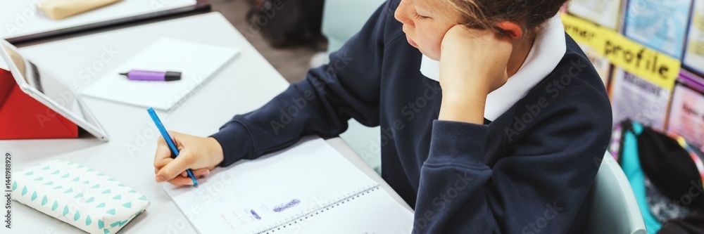 Fototapete Student writing in a notebook, focused on schoolwork. Classroom setting with a pencil case and tablet. Learning and education in a school environment. Education and knowledge.