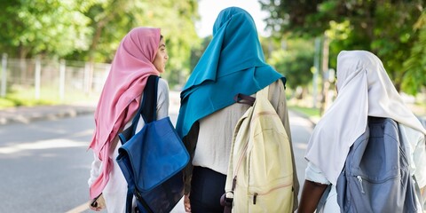 Three muslim girls walking outdoors with backpacks and colorful headscarves. They are enjoying a...
