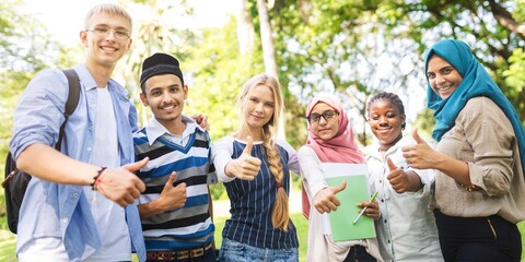 Diverse group of young students smiling and giving thumbs up. Multicultural high school students giving thumbs up. Diverse high school students in a park together.