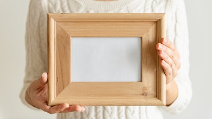 Person holding a wooden frame. The frame is empty, showcasing its wooden texture. Hands grip the wooden frame, emphasizing its simplicity and natural look. Woman holding a blank wooden frame.