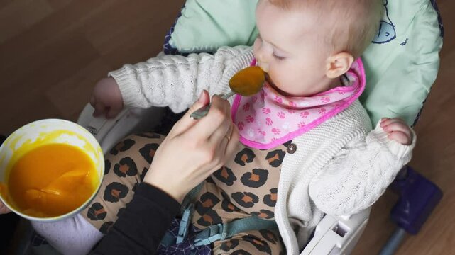 Baby being spoon-fed in high chair during mealtime, warm and calm indoor setting