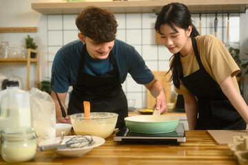 Man and woman wearing aprons and preparing breakfast together in the kitchen