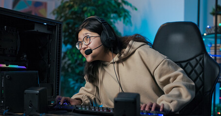 Focused female gamer wearing a microphone headset communicates with online rivals during a match,...