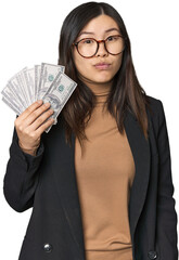 Chinese businesswoman with dollar bills shrugs shoulders and open eyes confused.