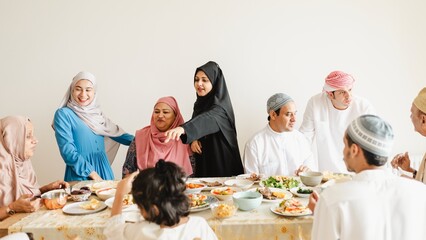 Muslim family enjoying a meal together. Diverse group sharing food. Family gathering around table. Smiling faces, lively conversation, shared meal. Muslim family celebrating end of fast, Ramadan feast