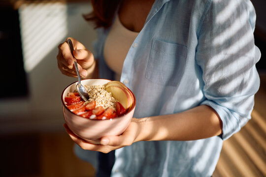 Close up of woman having oatmeal topped with fresh fruit at home.