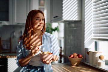 Smiling woman eating healthy food for breakfast in kitchen.