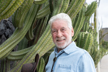 Portrait of an old smiling caucasian senior bearded man in outdoors holding a cowboy leather hat enjoying a walk in public park