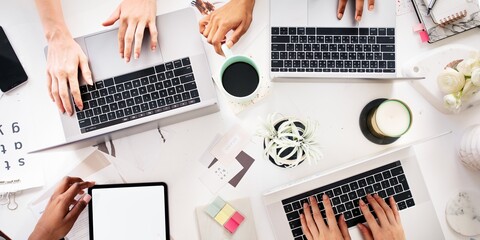Top view of diverse group of hands collaboratively working on laptops and a tablet. Top view of teamwork's hands working together with laptop and tablet. Top view of business team working together