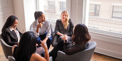 Group of diverse women having a meeting in a bright room. Diverse women discussing ideas. Diverse women sharing thoughts. Diverse women in a collaborative office meeting room.