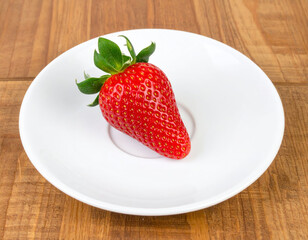 Fresh ripe strawberry on white plate, showcasing its vibrant red color and glossy texture, evokes sense of freshness and natural sweetness