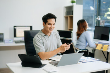 Confident business expert attractive smiling young man typing laptop and holding digital tablet on desk