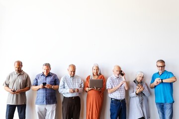 Group of diverse seniors using technology. Elderly men and women with devices. Seniors engaged with phones, laptops, and smartwatches against a white background. Diverse group of people using laptops.