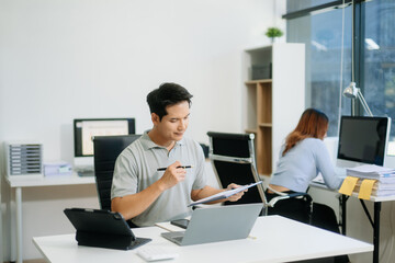 Confident business expert attractive smiling young man typing laptop and holding digital tablet on desk