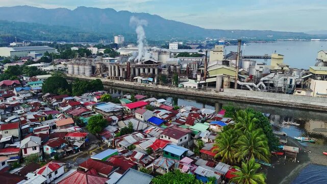 Distant view captures a coastal industrial complex belching smoke over shanty homes in Cagayan de Oro, Mindanao, Philippines, illustrating stark contrasts between industry and community.