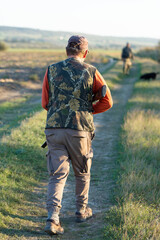 Mature hunter man holding a shotgun and walking through a field