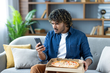 A man looks at his phone with a confused expression while holding a pizza box, possibly dealing with an order issue