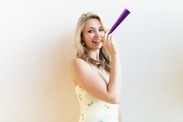 Smiling woman with blonde hair holding a purple party horn. Blonde woman in a festive mood. Party...