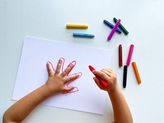 Child drawing hand outline with colorful crayons on white paper