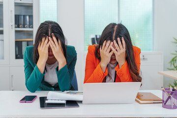 Two Asian businesswomen sit together at a desk, working professionally to solve problems. One...