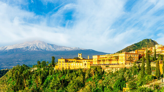 Amazing landscape of a beautiful mountain town Taormina in Sicily, Italy. Scenic view from a green mountain to a beautiful famous hotel and high majestic mount vulcan Enta in snow.