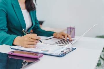 Two Asian businesswomen sit together at a desk, working professionally to solve problems. One...