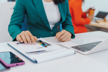 Two Asian businesswomen sit together at a desk, working professionally to solve problems. One appears to be the boss