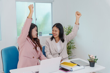 Two Asian businesswomen working together at a desk, focused and professional. They collaborate on...