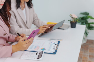 Two Asian businesswomen working together at a desk, focused and professional. They collaborate on...