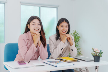 Two Asian businesswomen working together at a desk, focused and professional. They collaborate on...