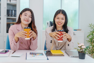 Two Asian businesswomen working together at a desk, focused and professional. They collaborate on...