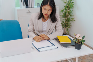 Two Asian businesswomen working together at a desk, focused and professional. They collaborate on...