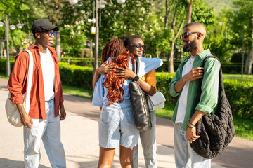 Excited happy group of African university students cheerfully greeting one another with hugs outside in park. Black friends congratulating of finals, laughter clapping, friendly meeting together 